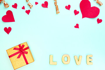 Gold Word Love with red paper hearts, gift, confetti on blue background. Sweet holiday background and small hearts.