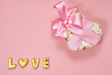 Fototapeta na wymiar Heart shaped Valentines Day gift box with pink curved ribbon and gold word love on paper background. Top view, flat lay.