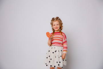 portrait of a girl a blonde child with a Lollipop on a stick smiling in colored clothes on a white background