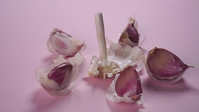 The husks and cloves of garlic are beautifully laid with a pattern on a delicate pink background. Dolly shot. Spicy vegetables for seasoning