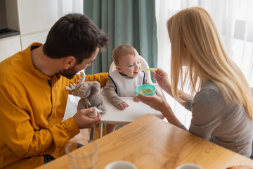 Father and mother feeding their son in the kitchen at home