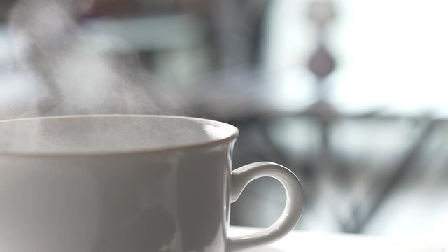 Steaming hot cup of coffee or tea in a cafe in the morning for breakfast. Backlit shot and sun rays. 