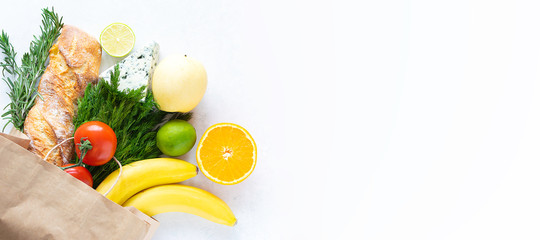 Fresh organic vegetables, fruit, herbs and cheese in reusable paper bag on white marble background. Long banner format. Eco shopping concept. Healthy food concept, copy space for your design.