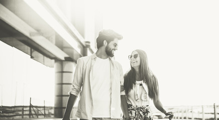 The young bearded man and his beautiful girlfriend are on a journey. They are stylishly dressed and have sunglasses. They are happy and laughing. Black and white photo.