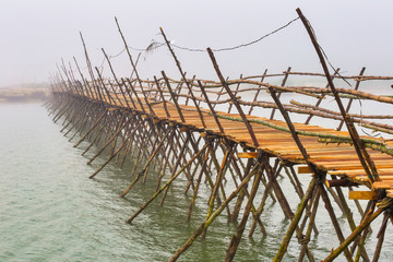 Wooden bridge across the misty river. Hoi An, Vietnam