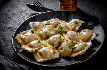 Meat dumplings - russian pelmeni, ravioli with meat in black plate on Dark grey black slate background