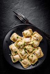 Meat dumplings - russian pelmeni, ravioli with meat in black plate on Dark grey black slate background