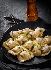 Meat dumplings - russian pelmeni, ravioli with meat in black plate on Dark grey black slate background