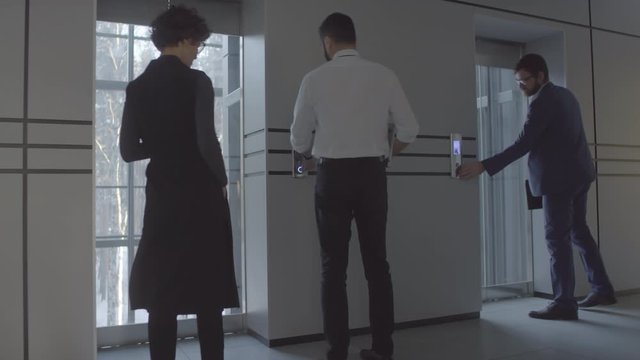 Medium shot of confident businesspeople talking and walking into glass elevator in modern office building. Unrecognizable businessman riding scooter along hallway