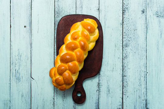 fresh challah bread on cutting board, blue wooden table, top view
