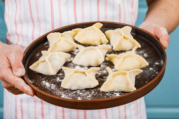 The cook holds a tray of dumplings. Homemade food.