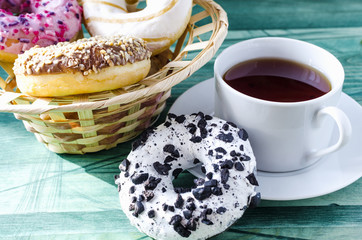 bright pink, white and brown doughnuts and a Cup of tea in a white bowl on a green wooden background