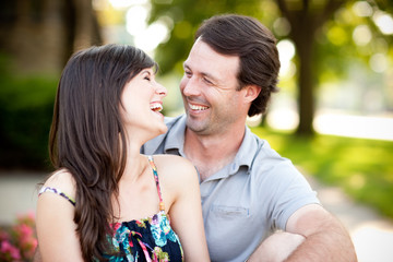 Happy Young Man and Woman Laughing While Sitting on Sidewalk