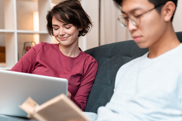 Photo of pleased multinational couple reading book and using laptop