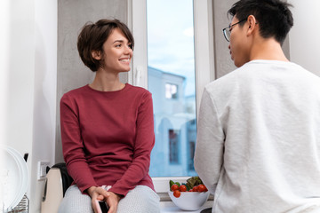 Photo of smiling multinational couple using cellphone and cooking dinner