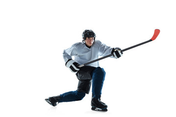 Serious. Young male hockey player with the stick on ice court and white background. Sportsman wearing equipment and helmet practicing. Concept of sport, healthy lifestyle, motion, movement, action.