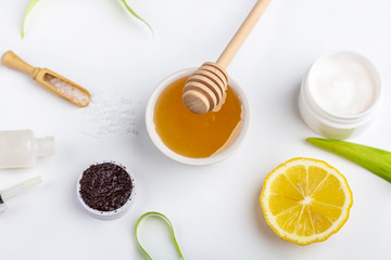 Natural organic ingredients homemade skin care. Cleansing and nourishing cosmetic. Beauty products: cream, honey, coffee scrub,  among green leaves on white background. Close up, copy space for text