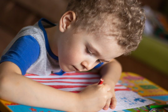 Little boy draws a USA flag. The boy colors the flag with crayons. Education, the study of state symbols, a photo.