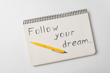 Follow your dream motivation notice. Notepad and pen on white background.