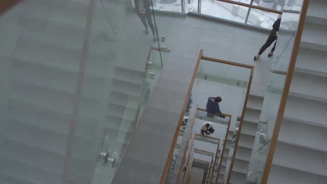 High angle PAN shot of busy staircase in modern multi-story office building. Businesspeople in formalwear walking up and down stairs