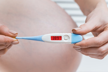 Pregnant woman with a electronic thermometer. High temperature, disease during pregnancy concept