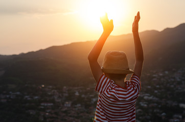 Fototapeta premium Back view, boy raised his hands to meet the sun. Kid on sunset background