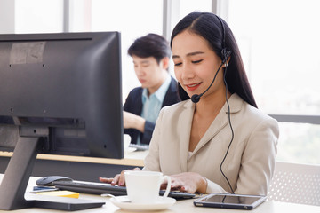 Smiling Asian call center operator work in office and talk to customer.