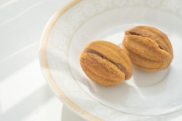 Two small cookies walnuts on a white saucer and a sunny table