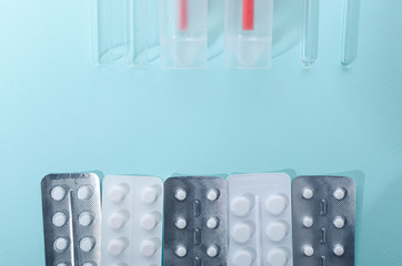 Top view of lab glass rods, plastic urine container for tests, silver and white blister packs, drugs on the blue background.Empty space for test