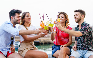 Friends toasting, saying cheers holding tropical blended fruit cocktails. Young people having fun...