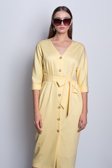 Fashion model in big sunglasses wearing yellow dress with buttons posing over gray background