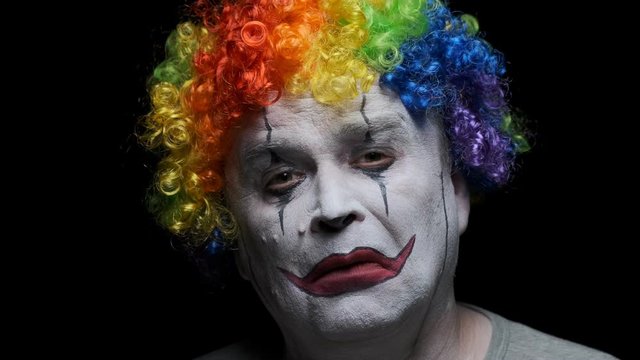 Portrait of evil male clown grimaces while looking at camera on black background.