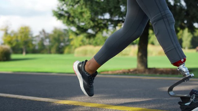 Disabled woman jogging in park. Fit girl in sportswear training in green park