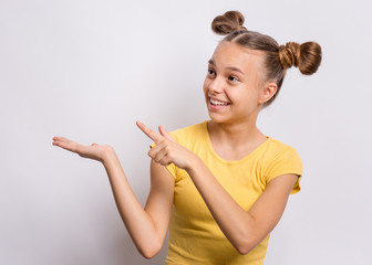 Portrait of teen girl pointing finger away at copyspace, on gray background. Beautiful caucasian young teenager smiling and attracted by attention pointing finger at something. Happy child. - 326416032