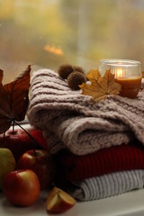 Obraz na płótnie Canvas Autumn layout of woolen things, a lighted candle and apples on the windowsill
