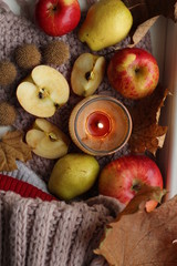 Top view on a candle, ripe apples, a dry leaf and a knitted scarf
