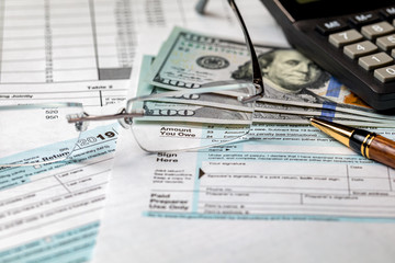 1040 income tax return form 2019 with calculator, money, and pen. Focus through glasses on amount you owe. Concept of filing taxes, payment, refund, and April 15, 2020 tax deadline