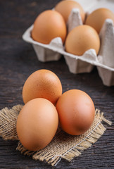 Raw eggs in egg box on rustic wooden background.