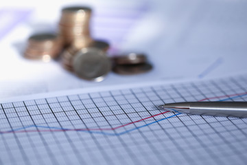 Silver pen lies on report with graph next to coin. Scaling business helps capture market and...