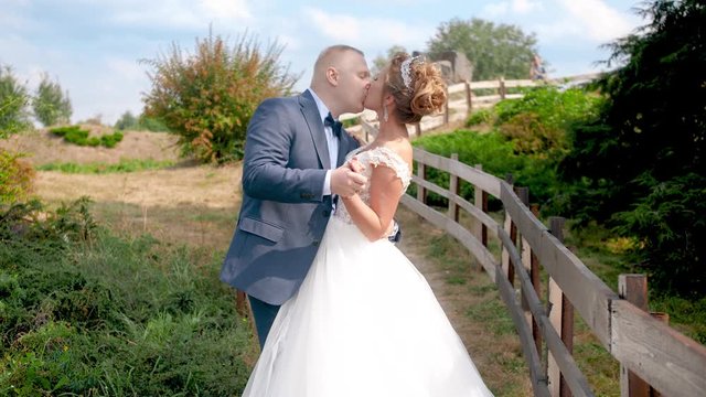 4k slow motion video of happy newly married couple dancing and kissing next to long wooden fence in the country