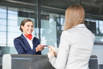 Passenger service agent giving woman's passport and boarding pass in check in area at airport