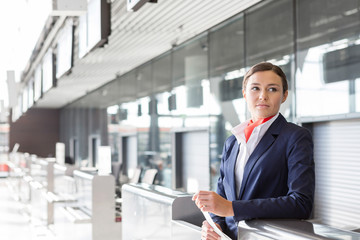 Portrait of young attractive passenger service agent holding boarding pass in airport check in area