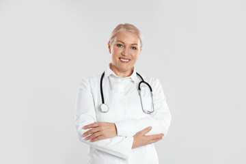 Portrait of mature doctor with stethoscope on light grey background