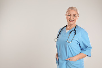 Portrait of mature doctor with stethoscope on light grey background. Space for text