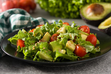 Salad with avocado, lettuce, tomato and flax seeds on black plate