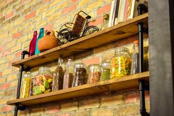 Spices and food in transparent jars with books on a shelf on a brick wall