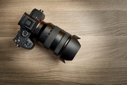 top view of a modern digital mirrorless full-frame camera with attached zoom lens and hood on wooden table