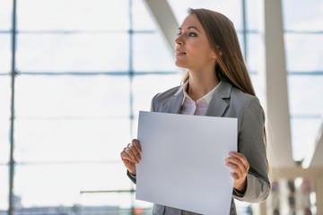Portrait of businesswoman standing while holding blank white board in arrival area at airport