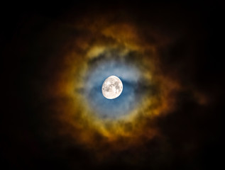Naklejka na ściany i meble Moon, almost full, shining through clouds creating a vibrant and colorful halo. Natural phenomenon. Beautiful and scenic skyscape. Scenic cloudscape at night.