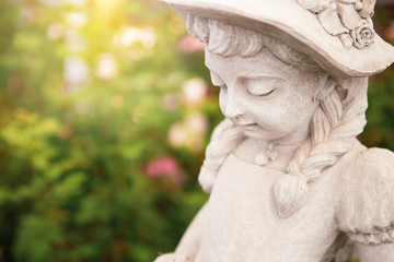 Closeup girl statue over blurred flower garden background, vintage outdoor warm light, garden design and decoration item